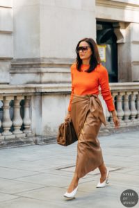 mujer con jersey naranja y falda marron